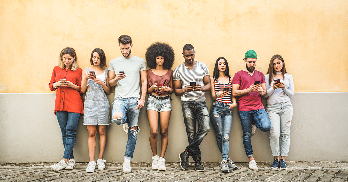 A group of Gen Z young people standing along a wall looking at their cell phones.