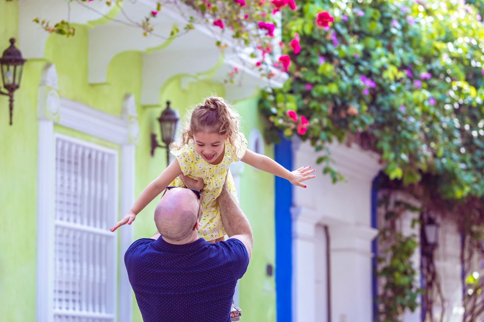 A photo of Ludo, author of the blog post, lifting his child up, who is smiling at him. In the background there are brightly colored houses and flowers.